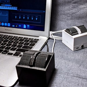 Könnte beinhalten: Zwei schwarze und weiße Fußpedale, die an einen Laptop angeschlossen sind. Die Pedale haben eine strukturierte Oberfläche und sind mit einem weißen Kabel an den Laptop angeschlossen. Der Laptop-Bildschirm zeigt ein Musikprogramm mit einer Tastatur und anderen Steuerelementen.