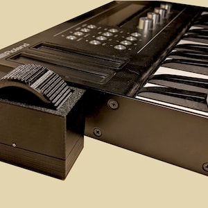 May include: A black Roland synthesizer with a white keyboard and a black foot pedal attached to the side.