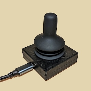 Pode incluir: Um joystick USB preto com uma parte superior de borracha e um cabo preto.