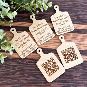May include: Five wooden cutting board-shaped business cards. Each card has the text "The Slice is Right Charcuterie, Jane Smith, Owner, 555.123.4567, TSIRCharcuterie.com, @Thesliceisright." Two cards feature a QR code.