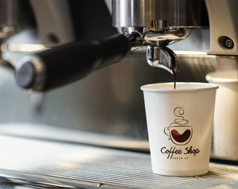 Könnte beinhalten: Nahaufnahme einer Kaffeemaschine, die Espresso in einen weißen Pappbecher mit dem aufgedruckten Logo "Coffee Shop Cheer Up" gießt.