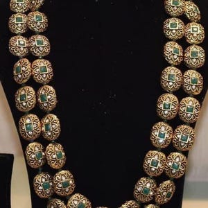 Könnte beinhalten: Eine goldene Halskette mit grünen und weißen Steinen. Die Kette besteht aus runden, verzierten Gliedern.