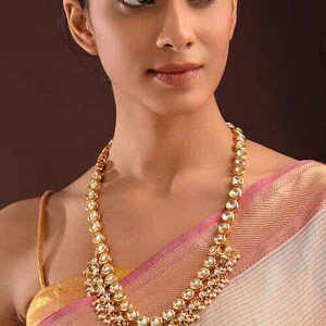 May include: A gold necklace with white stones and pearl accents. The necklace has a layered design with a central pendant and dangling pearl drops.