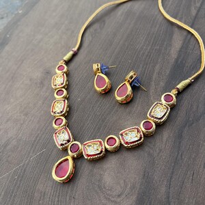 May include: A gold necklace with a red teardrop pendant and red square stones. Matching earrings with red teardrop stones.