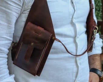 May include: A brown leather crossbody bag with a flap closure and a small pocket on the front. The bag is worn over a white shirt.
