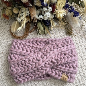 Può includere: Un cerchietto in maglia morbida rosa con un design intrecciato. Il cerchietto ha un piccolo cartellino in pelle marrone con il testo "Small Wonders Knit Co."