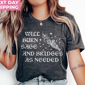 Puede incluir: Una camiseta gris oscuro con texto blanco que dice "Will burn sage and bridges as needed". El texto est&aacute; acompa&ntilde;ado por una ilustraci&oacute;n estilizada de un manojo de salvia ardiente con estrellas.
