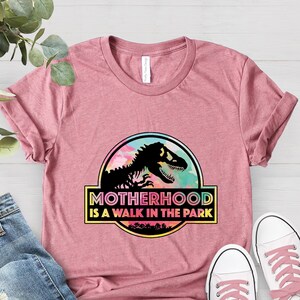 Puede incluir: Camiseta rosa con un gr&aacute;fico de un dinosaurio y el texto "Motherhood is a walk in the park".