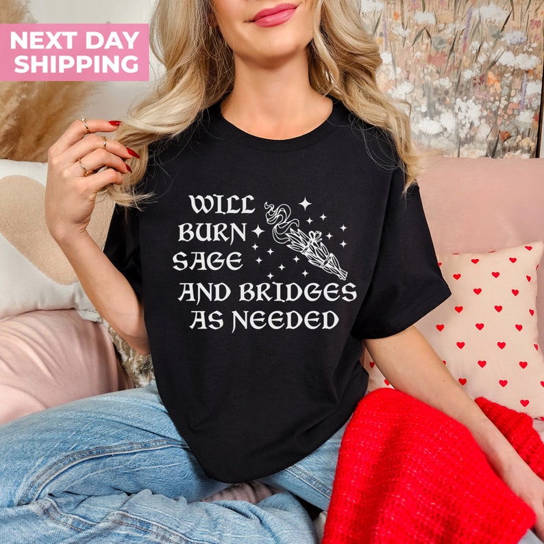 Puede incluir: Camiseta negra con texto blanco que dice "Will burn sage and bridges as needed". El texto est&aacute; acompa&ntilde;ado por un gr&aacute;fico blanco de un manojo de salvia ardiente.
