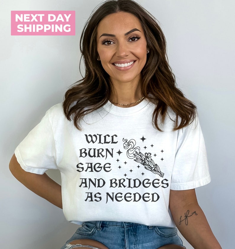 Puede incluir: Camiseta blanca con texto negro que dice "Will burn sage and bridges as needed" con una peque&ntilde;a ilustraci&oacute;n de un manojo de salvia ardiente.