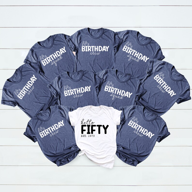 May include: A set of nine navy blue t-shirts with white text that reads "fifty birthday crew" and "fifty birthday squad". One white t-shirt with black text that reads "hello fifty est. 1973".