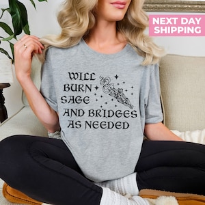 Puede incluir: Camiseta gris con el texto "Will burn sage and bridges as needed" y una ilustraci&oacute;n en blanco y negro de un manojo de salvia ardiente.
