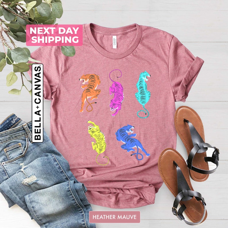 Puede incluir: Una camiseta de color malva con un gr&aacute;fico de cinco tigres coloridos. Los tigres est&aacute;n en diferentes poses y est&aacute;n delineados en negro. La camiseta est&aacute; hecha de un material suave y c&oacute;modo y es perfecta para el uso diario.