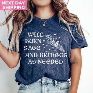 Puede incluir: Una camiseta azul marino con texto blanco que dice "Will burn sage and bridges as needed". El texto est&aacute; en una fuente estilizada y est&aacute; acompa&ntilde;ado por un gr&aacute;fico de un manojo de salvia ardiente con humo y estrellas.