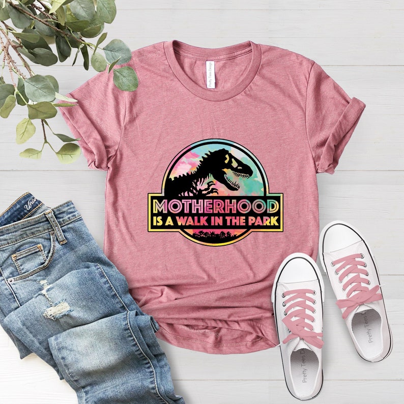 Puede incluir: Camiseta rosa con un gr&aacute;fico de un dinosaurio y el texto "Motherhood is a walk in the park".