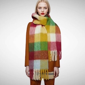 May include: A colorful plaid scarf with fringe. The scarf is made of a soft, fuzzy material and features a variety of colors, including red, yellow, green, and blue.