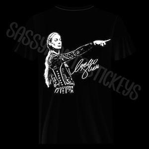 May include: A black t-shirt featuring a white graphic print of a person with long hair pointing to the right. The design includes a star-patterned jacket and a signature. The text SASSY STICKERS is visible in the background in a light gray font.