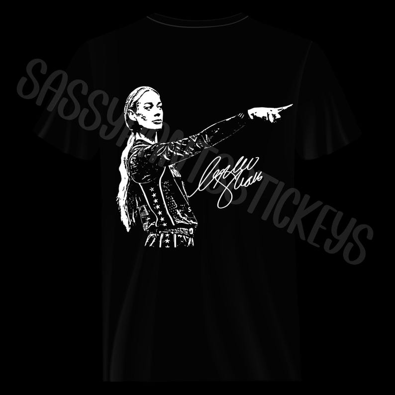 May include: A black t-shirt featuring a white graphic print of a person with long hair pointing to the right. The design includes a star-patterned jacket and a signature. The text SASSY STICKERS is visible in the background in a light gray font.