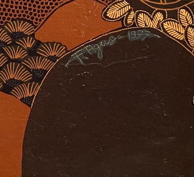 Op de afbeelding: Close-up van een gedeelte van een schilderij met een donkerbruine achtergrond. Het schilderij heeft oranje en zwarte waaiervormige patronen en gouden accenten. De handtekening van de kunstenaar en het jaar 1952 zijn zichtbaar.