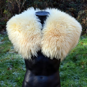 Puede incluir: Un cuello de piel de oveja blanca con una textura esponjosa. El cuello se muestra en un maniquí negro.