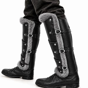 May include: Black knee-high boots with silver buckles and gray faux fur trim. The boots have multiple straps and decorative silver studs. The boots are made of a leather-like material and are designed for a medieval or fantasy aesthetic.