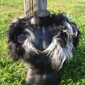 May include: A black and white faux fur shoulder piece with brown leather accents and a gold chain. The leather pieces are round with a floral design and small silver studs. The shoulder piece is displayed on a black mannequin.