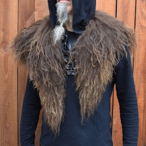 Könnte beinhalten: Ein brauner Kunstfellkragen mit langen, zotteligen Strähnen. Der Kragen wird über einem schwarzen Kapuzenpullover mit einem schwarzen Shirt darunter getragen.