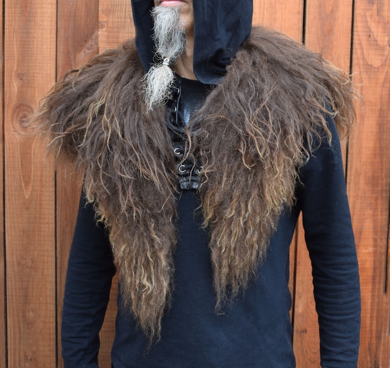 May include: A brown faux fur collar with long, shaggy strands. The collar is worn over a black hooded sweatshirt with a black shirt underneath.