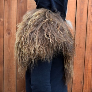 May include: A brown and blonde faux fur shoulder piece. The fur is long and shaggy, and the piece is worn over a black hooded sweatshirt.