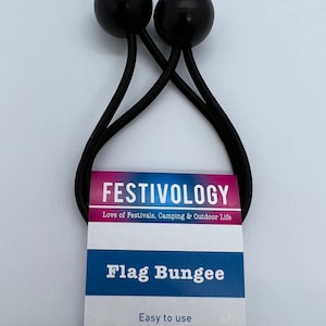 May include: Black flag bungee with two black rubber balls on the ends. The bungee is attached to a white card with the text "FESTIVOLOGY Love of Festivals, Camping & Outdoor Life Flag Bungee Easy to use Secure flag attachment Low tension".