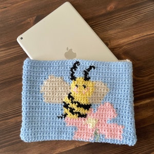May include: A blue crocheted pouch with a bee and flower design. The bee is yellow with black stripes and has a white face. The flower is pink with white accents.