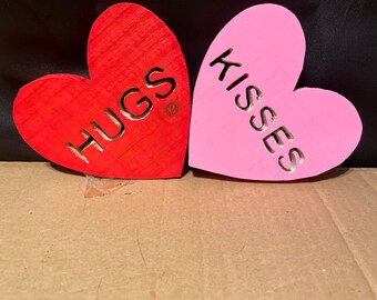 May include: Two wooden heart-shaped signs, one red with the word "HUGS" and one pink with the word "KISSES".
