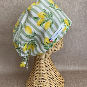Peut inclure: Une charlotte de bloc opératoire ornée d'un motif de citrons jaunes et de feuilles vertes sur un fond à rayures verticales vert clair et blanc. Elle comporte une étiquette blanche avec le texte LesCreationsNik et un petit drapeau français.