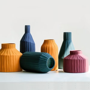 May include: Six ceramic vases in various colours and shapes. The vases are all textured with vertical lines. The colours are mustard yellow, dark blue, teal green, and burgundy.