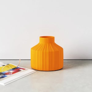 May include: A bright orange ceramic vase with a ribbed design. The vase is sitting on a grey surface.