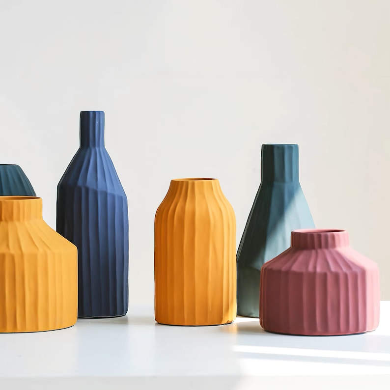 May include: Five ceramic vases in different colours and designs. The vases are all ribbed and have a modern, minimalist style. The colours are blue, yellow, and pink.