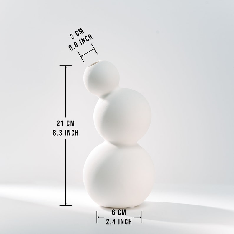 Może przedstawiać: Biały ceramiczny wazon o unikalnym, zaokrąglonym, tr&oacute;jstopniowym wzorze. Wazon ma 21 cm wysokości i 6 cm szerokości.