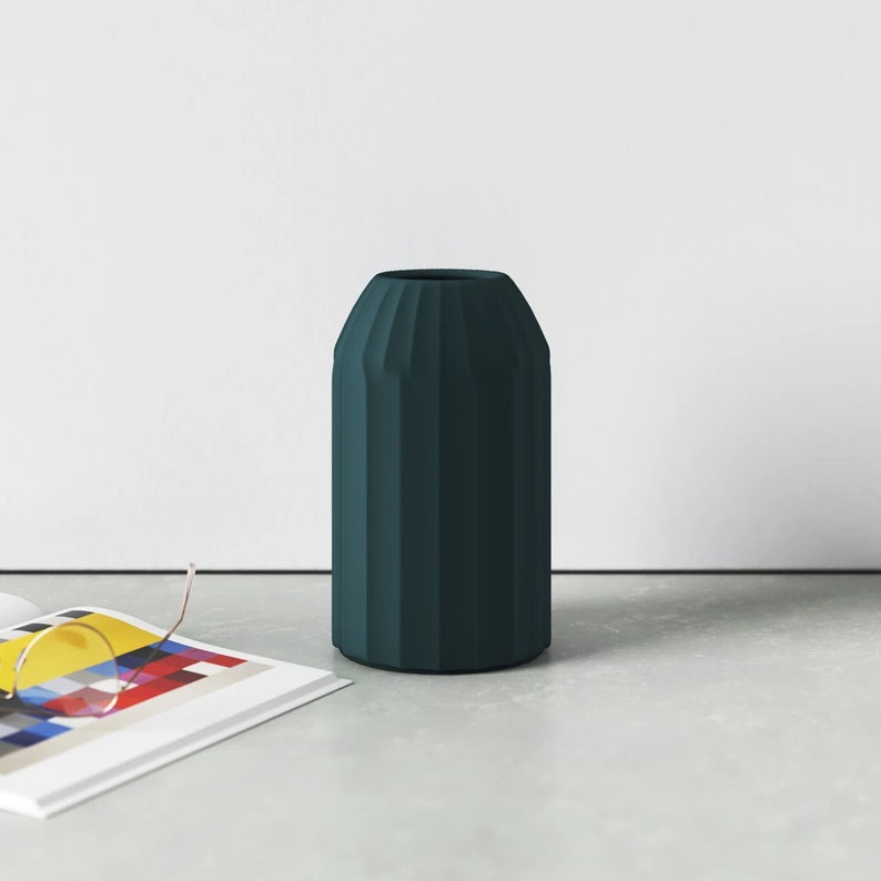 May include: A dark teal ceramic vase with a geometric, ribbed design. The vase is tall and narrow, with a rounded base and a slightly flared opening.