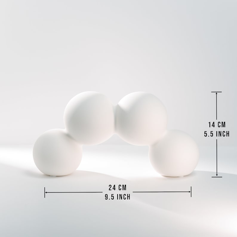 Może przedstawiać: Biała ceramiczna rzeźba z czterech połączonych kul tworzących łuk. Rzeźba ma 24 cm szerokości i 14 cm wysokości.