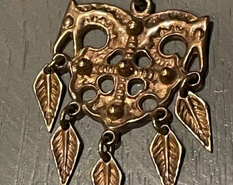May include: A vintage gold-toned pendant necklace. The pendant has an ornate, openwork design with a central motif and dangling leaf-shaped charms. The necklace is suspended from a delicate chain.