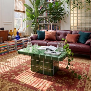 May include: A stylish living room featuring a burgundy leather sofa, a green tiled coffee table, and a patterned red rug. The room is decorated with plants, books, and vases. Natural light enters through a skylight and windows with wooden blinds.