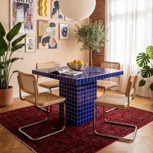 Könnte beinhalten: Esszimmer mit einem quadratischen, blau gefliesten Tisch und Korbstühlen. Ein roter, gemusterter Teppich liegt auf dem Boden. Die Wände sind pfirsichfarben, mit Kunstwerken. Über dem Tisch hängt eine große Papierlaterne.