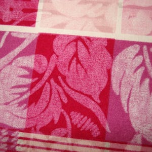 May include: Close-up of a fabric with a repeating pattern of squares. The squares feature a floral design in shades of pink and red. The fabric has a textured appearance, with a white grid pattern separating the squares.