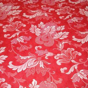 May include: Red fabric with a repeating floral pattern in white. The design features stylized flowers, leaves, and swirling vines. The fabric has a textured appearance, with the white elements standing out against the red background.