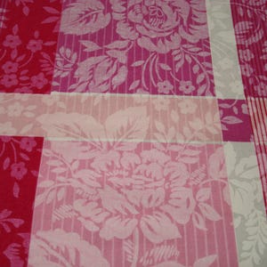 May include: Close-up of a fabric with a patchwork design. The fabric features a mix of floral and striped patterns in shades of pink, red, and white. The floral patterns include large roses and smaller flower clusters.