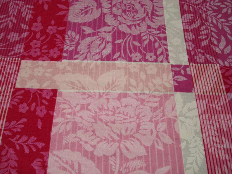 May include: Close-up of a fabric with a patchwork design. The fabric features a mix of floral and striped patterns in shades of pink, red, and white. The floral patterns include large roses and smaller flower clusters.