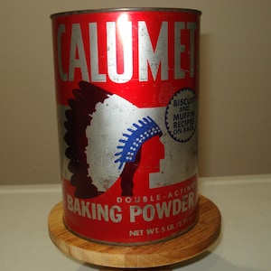 May include: A vintage Calumet Baking Powder tin. The red tin has the word "CALUMET" in silver. A Native American profile is on the front. The tin is on a small wooden stand. Net weight is 2.27 kg.