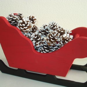 May include: A red wooden sleigh with black runners filled with pine cones dusted with white paint.