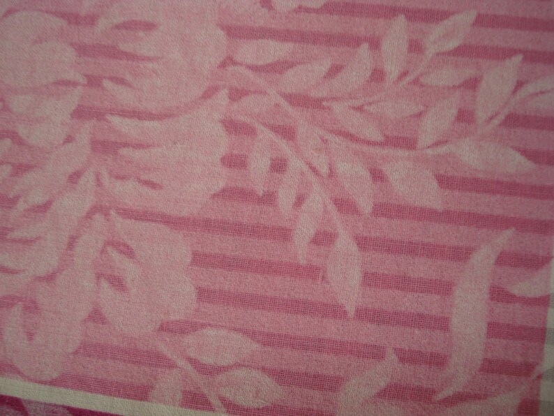 May include: Pink fabric with a floral and striped pattern. White floral and leaf silhouettes are set against a pink striped background. The fabric has a soft, textured appearance.