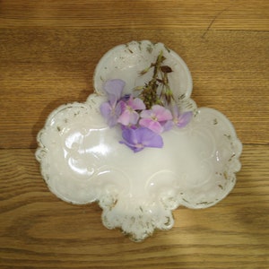 May include: A white ceramic dish with a decorative design, featuring a cluster of purple and white flowers.